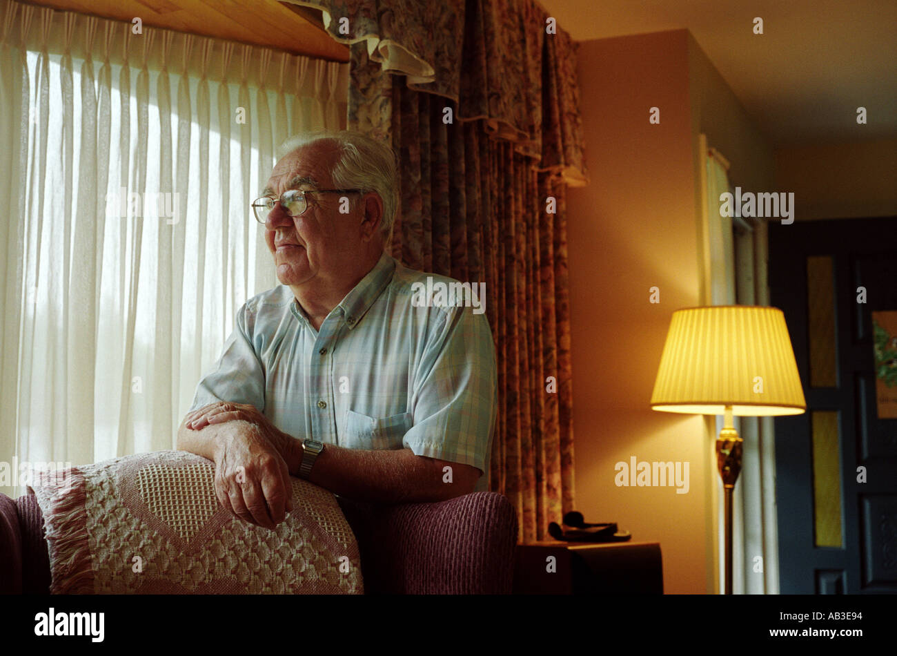 Alter Mann stützte sich auf den Stuhl und schaut aus dem Fenster in seinem New Brunswick Haus Stockfoto
