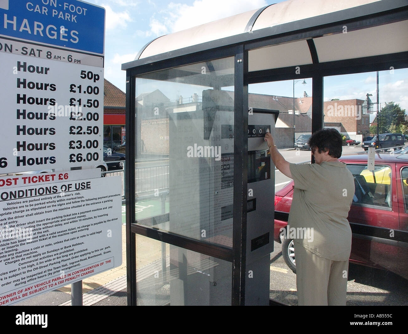 Reife Autofahrerin zahlt mit Münzen in Parkautomaten überdachte Kabine bei einem Gemeindeamt zahlen zu Fuß 2003 Parkschild Essex England UK Stockfoto