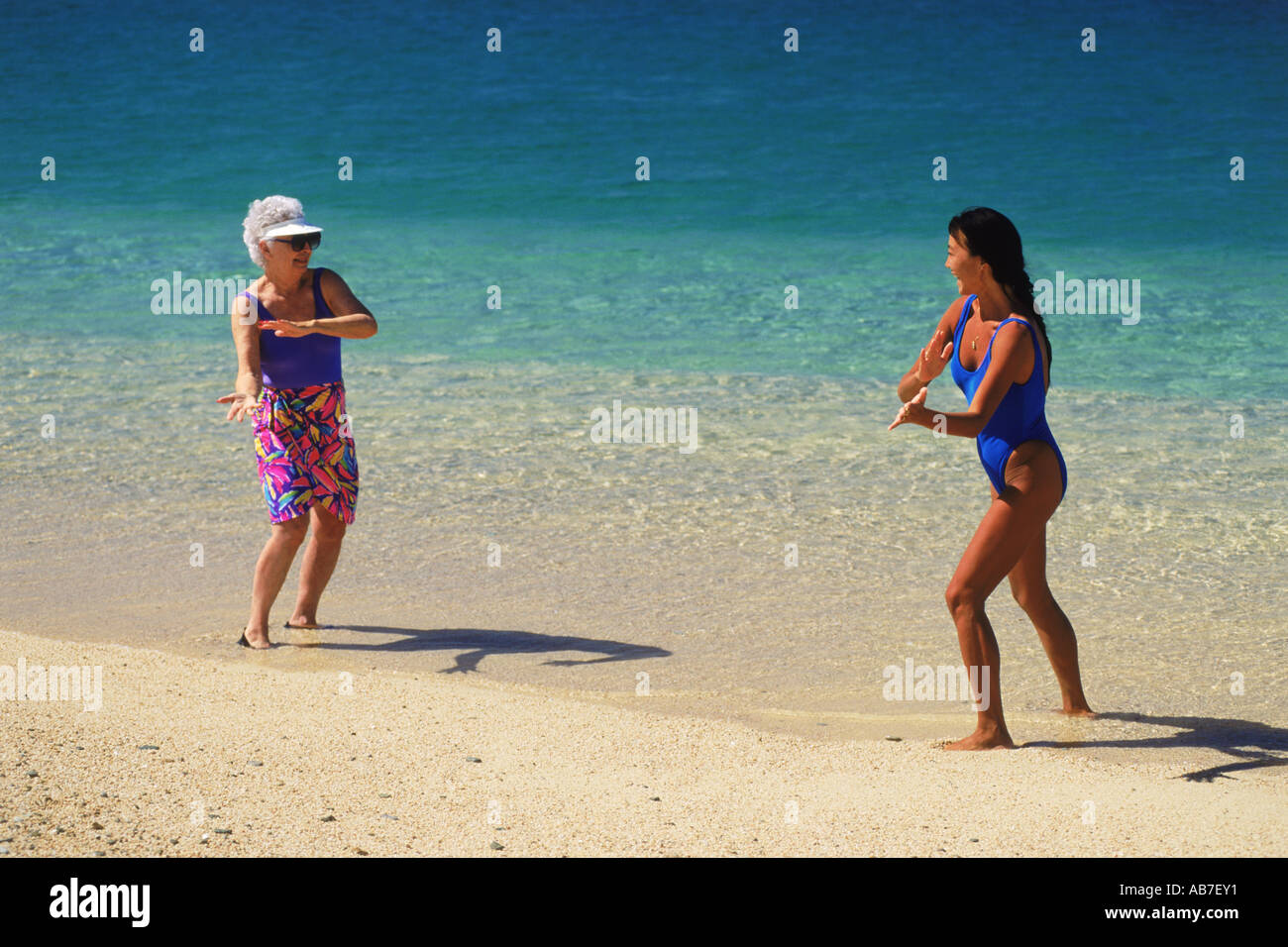 80 Jahre alte Großmutter und jüngere asiatische Frau Tai Chi und Yoga-Übungen am Sandstrand in Mexiko zu tun Stockfoto