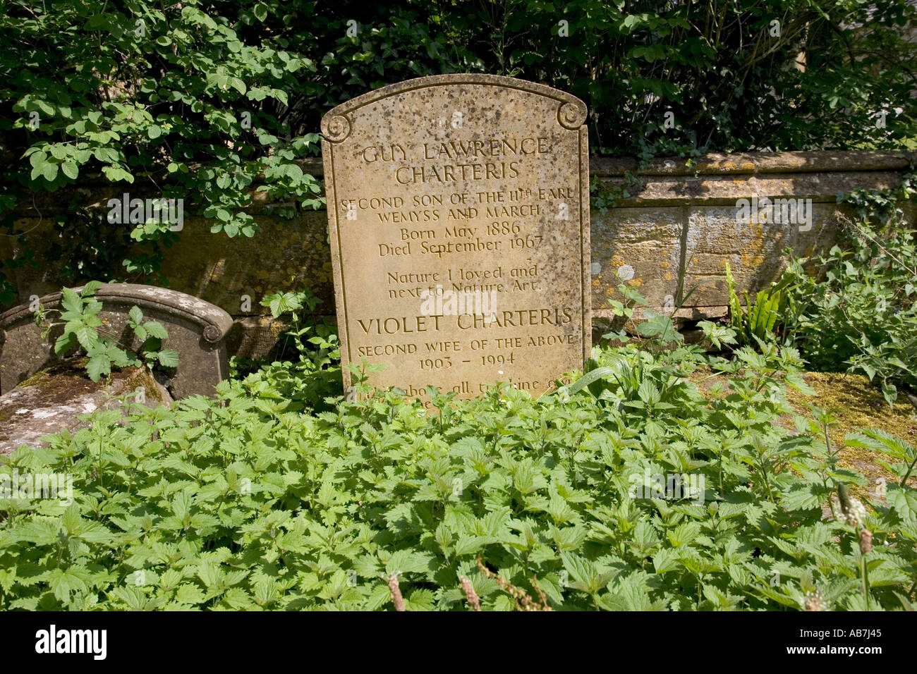 Brennesseln umgeben Grabstein von Guy Lawrence Charteris liebten Natur im Kirchhof Cotswolds UK Stockfoto