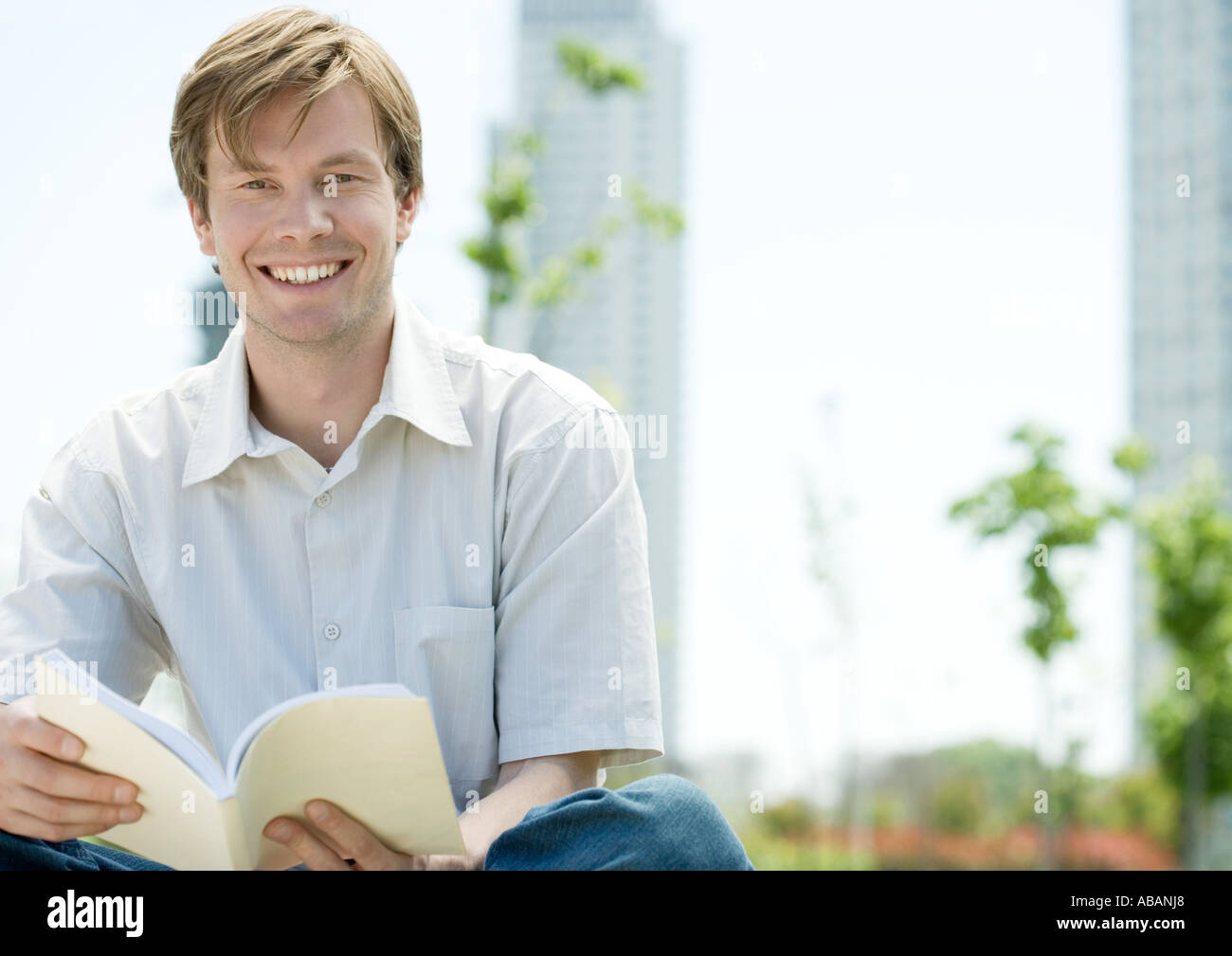 Mann sitzt im Stadtpark mit Buch Stockfoto
