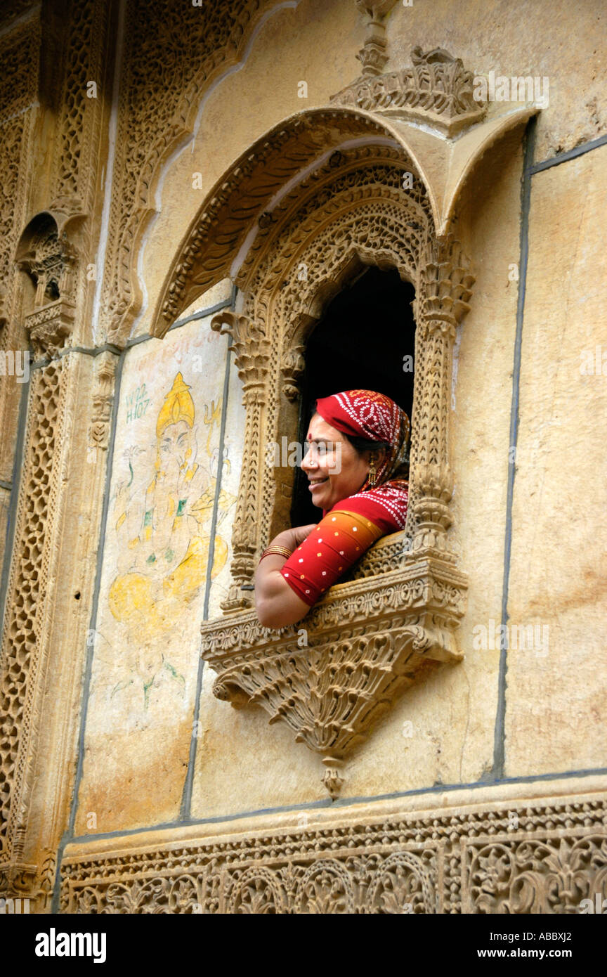 Indische Frau in roten Sari gekleidet sitzt in einem Fenster in der bildenden Kunst aus gelbem Sandstein Jaisalmer, Rajasthan Indien eingerichtet Stockfoto