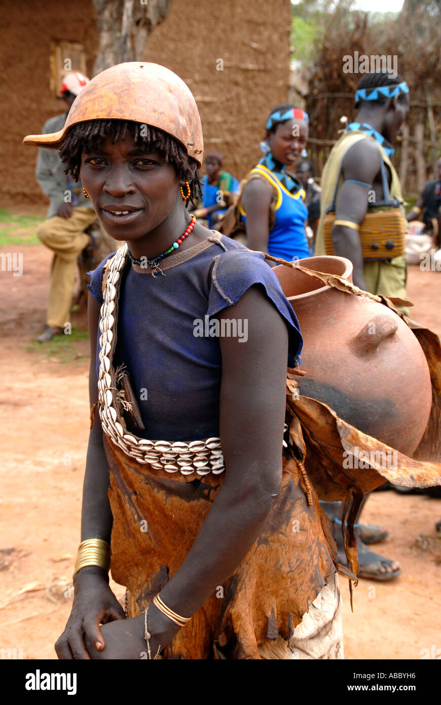 Frau trägt eine Kette von Kauri-Muscheln und eine Kalabasse auf dem Kopf trägt einen großen Tontopf auf dem Rücken auf dem Markt der Keyafer Stockfoto