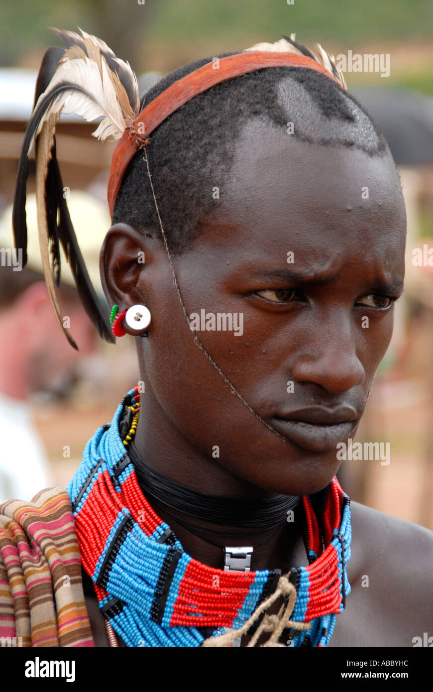 Porträt junger Mann des Volkes Banna mit Federn auf dem Kopf und bunte Halskette auf dem Markt der Keyafer Äthiopien Stockfoto