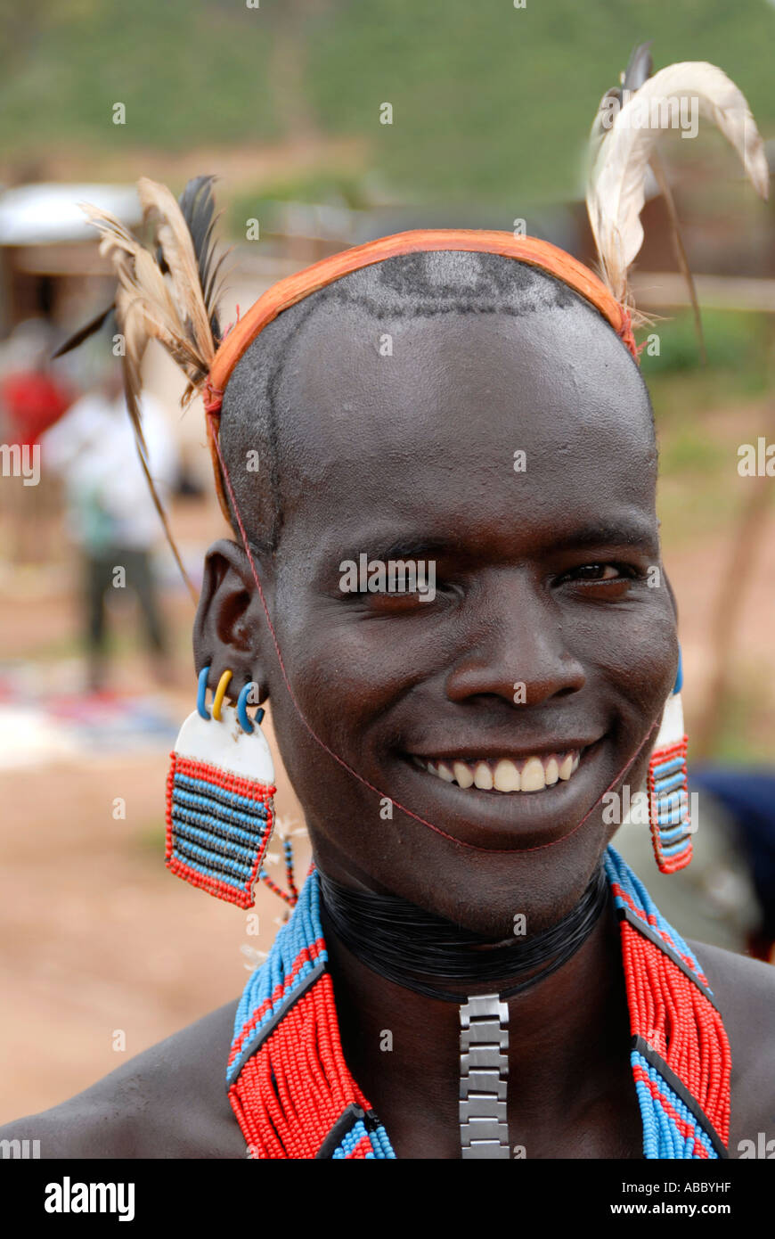 Porträt, lächelnde junge Mann des Volkes Banna mit Federn auf seinem Kopf bunte Halskette und bunten Ohr Dekoration auf der Stockfoto