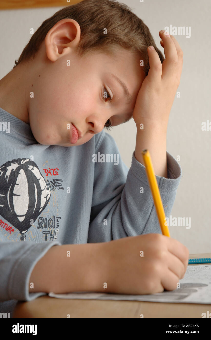 Jungen in ein blaues Hemd an einem Tisch sitzt und arbeitet mit Papier und Bleistift Stockfoto