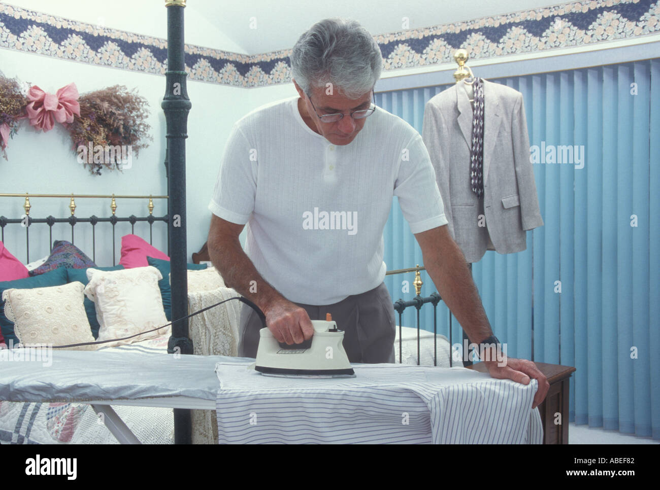 Älterer Mann ein Hemd bügeln im Schlafzimmer Self Care fähig. pov Herr © myrleen Pearson Stockfoto
