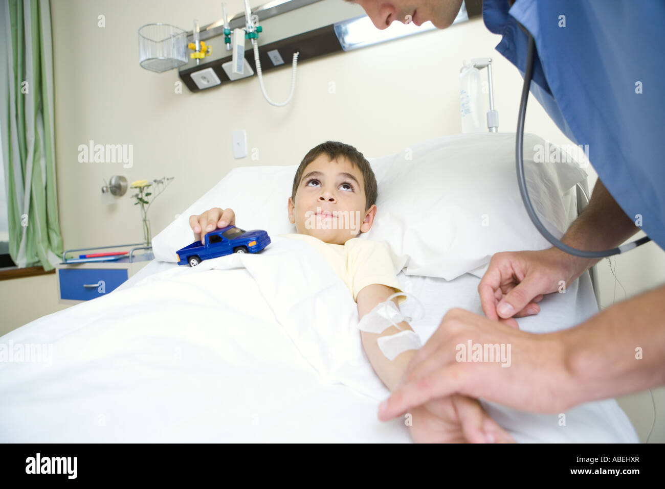 Junge im Krankenhausbett Spielzeugauto zu halten, während Intern Puls überprüft Stockfoto