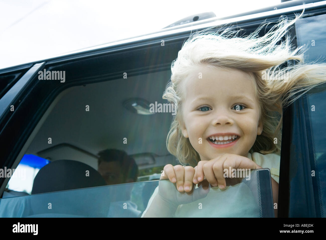 Kleines Mädchen in Auto, Blick aus Fenster, lächelnd in die Kamera, Haare im Wind wehen Stockfoto