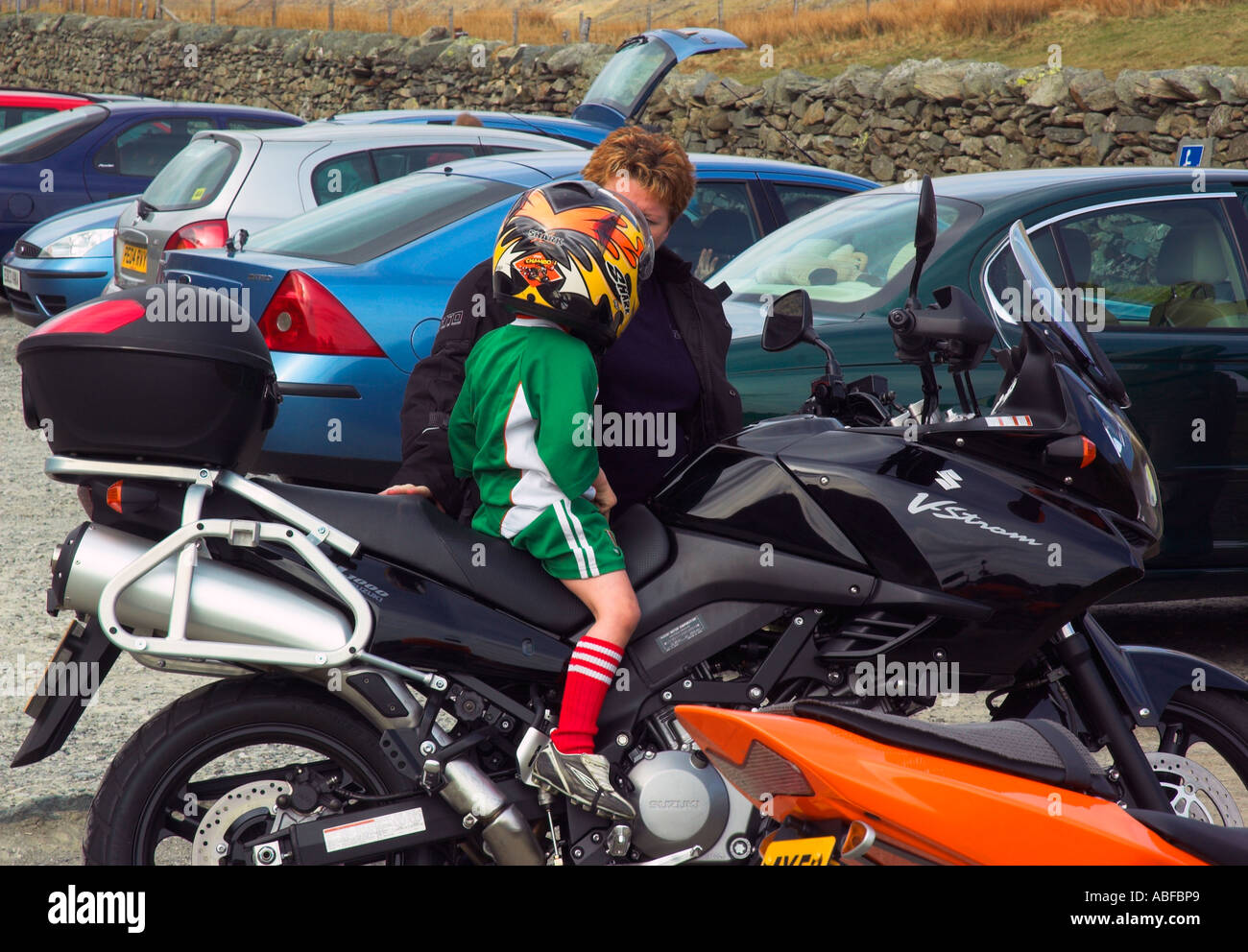 Ein kleiner Junge in Fußball-Streifen gekleidet und tragen einen riesigen Sturzhelm saßen auf einem Motorrad im Gespräch mit dem Eigentümer Stockfoto