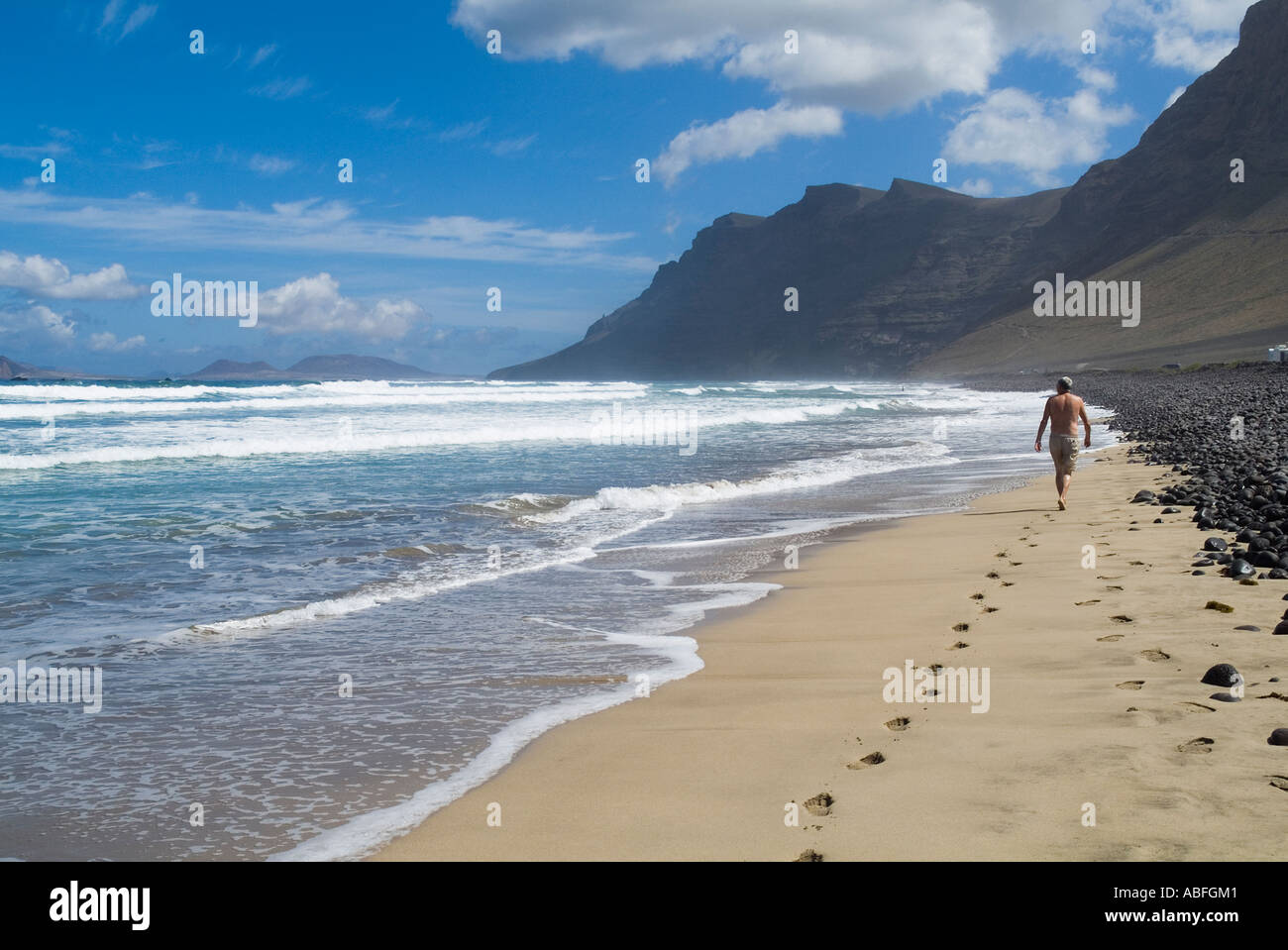 dh Playa de Famara FAMARA LANZAROTE Tourist Mann zu Fuß entlang Sandstrand El Risco Klippen und Bucht Schritte la caleta Strände Stockfoto