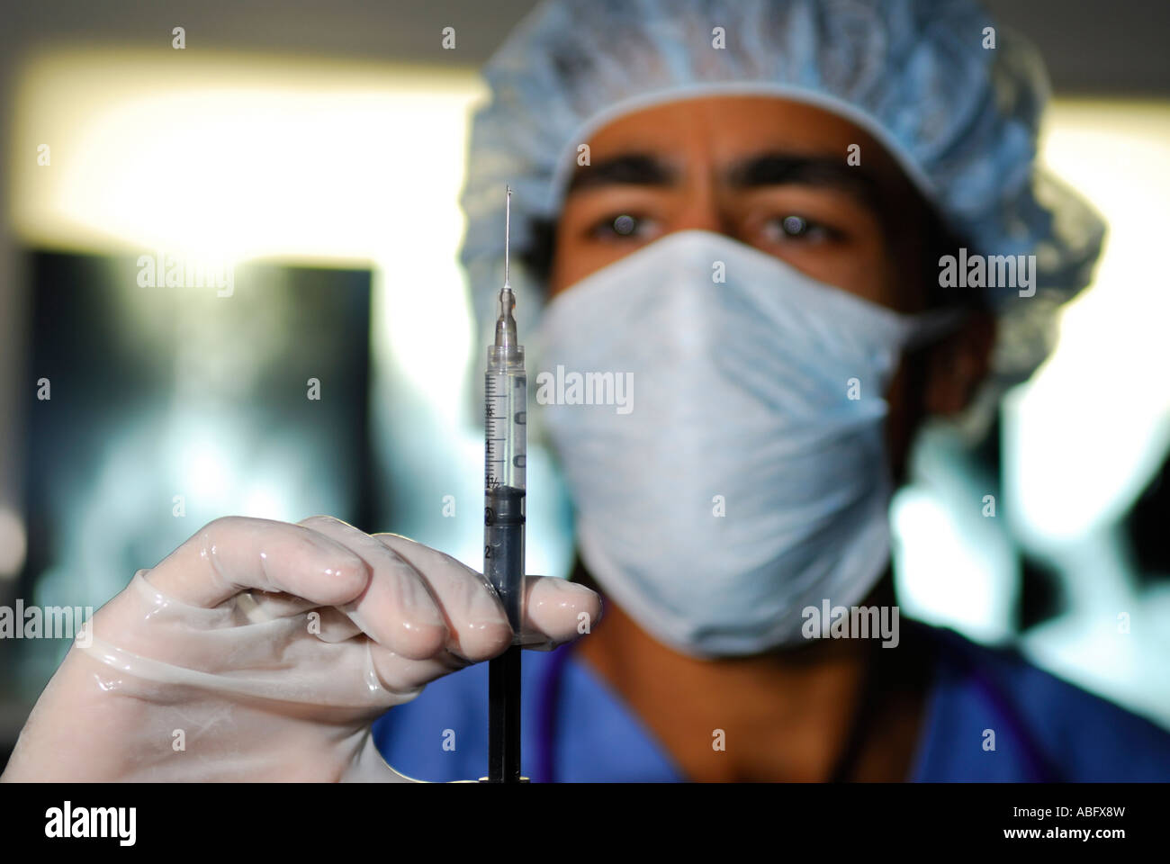 Arzt in Maske Haarnetz mit Handschuhen und Peelings mit Spritze in medizinische Klinik mit Xray Filme Stockfoto