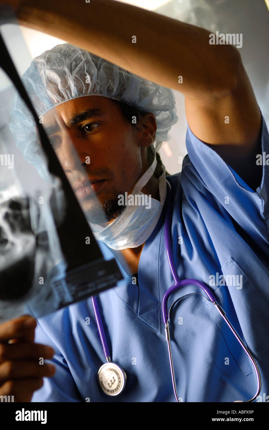 Junge schwarze Arzt mit Haarnetz und Maske Untersuchung medizinische Ergebnisse ein Xray-Transparenz-Film in einer Klinik mit gedrückter Stockfoto