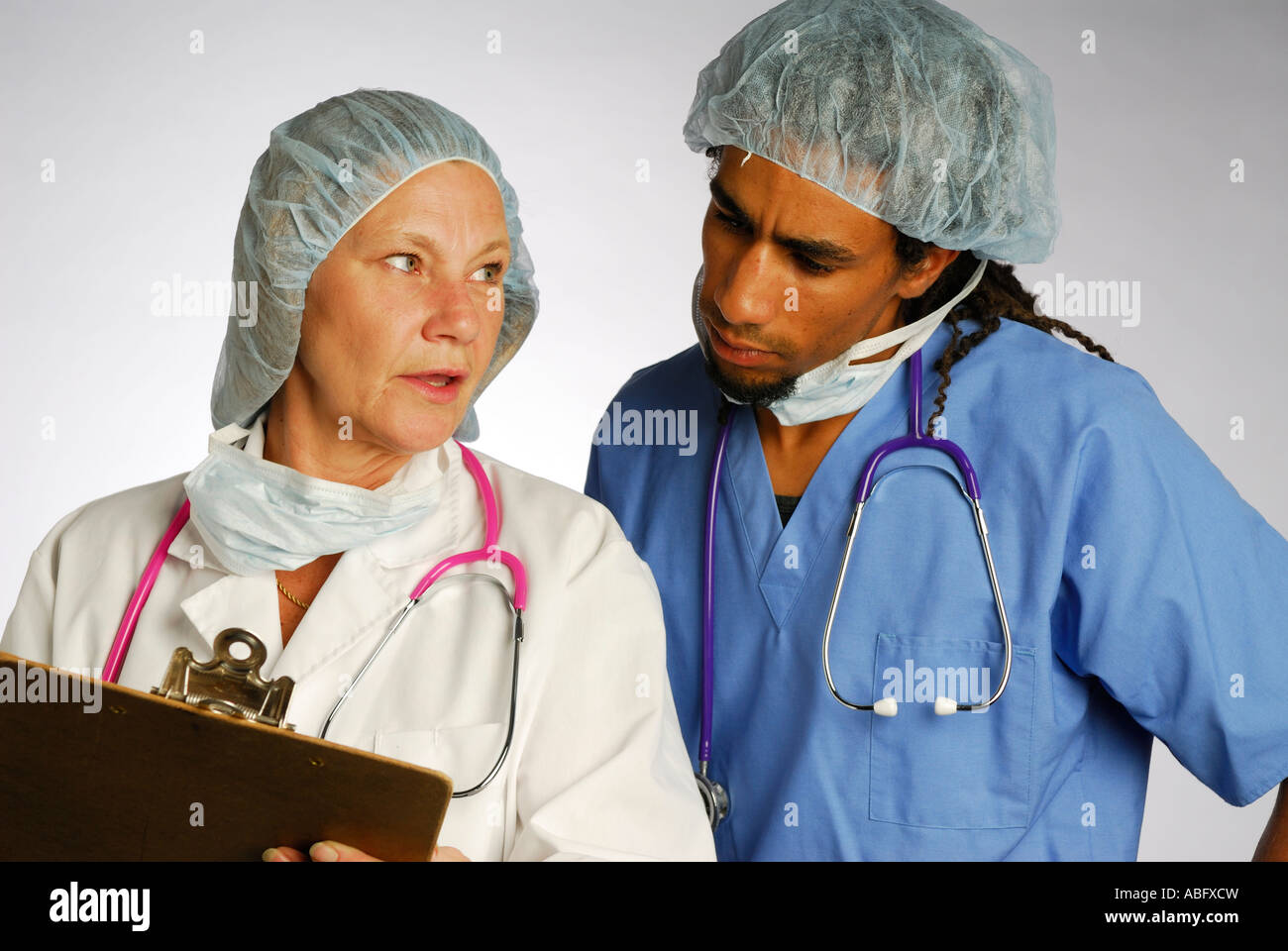 Weiblichen Oberarzt mit Diagramm auf Clip Board und Stethoskop Rücksprache mit jungen schwarzen Doktor im Haarnetz Stockfoto