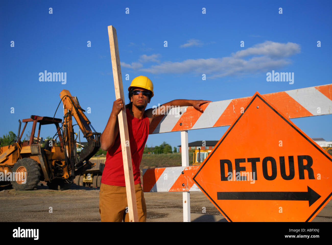 Bauarbeiter in Schutzhelm stützte sich auf ein Umweg Barriere Schild an einer Baustelle mit Bagger Bagger Stockfoto