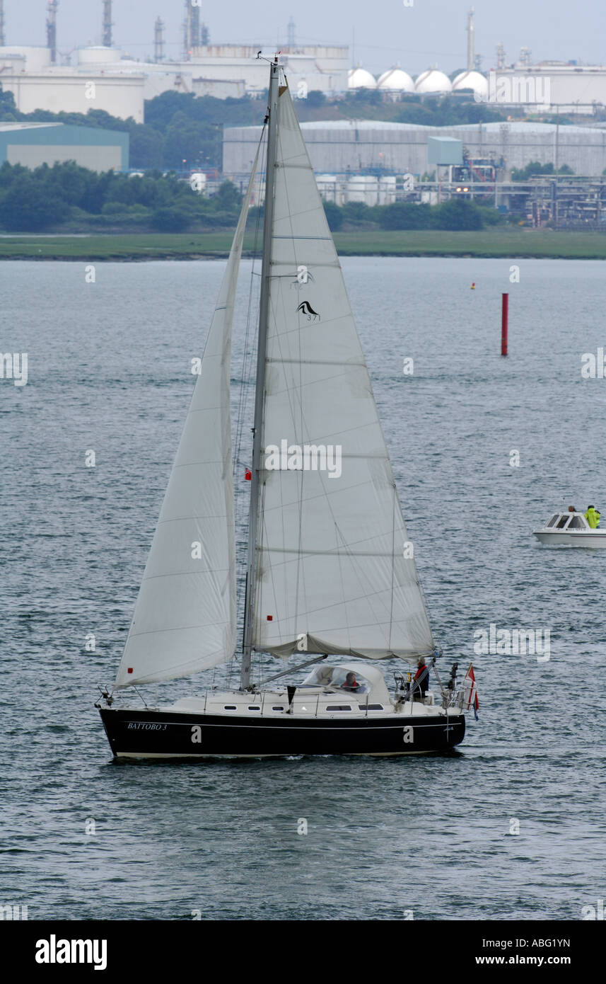 Segelyacht in Southampton Wasser mit Enichem Raffinerie im Hintergrund Stockfoto