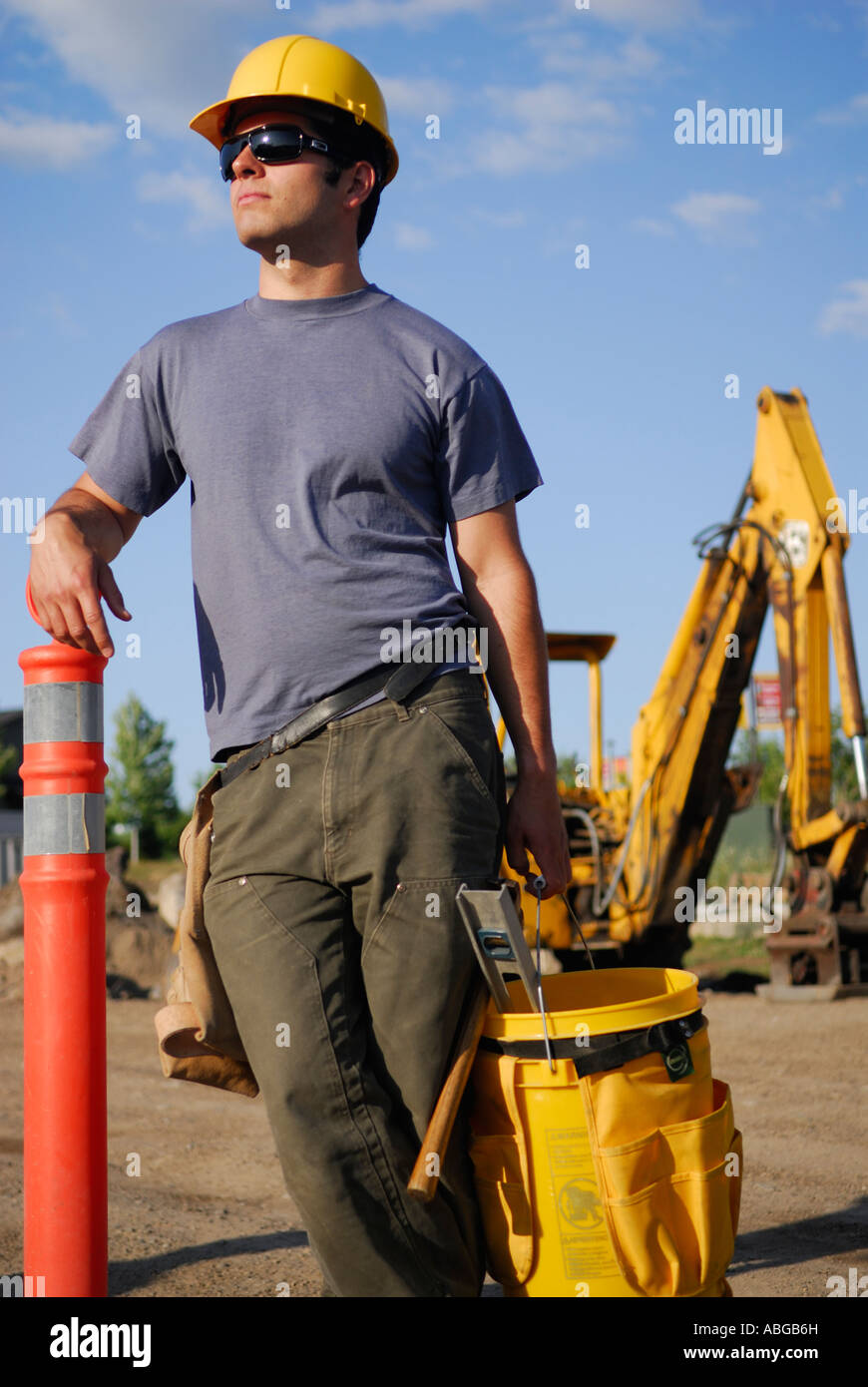 Junge männliche Bauarbeiter mit Schutzhelm anhalten mit Arbeit Eimer und Bagger im freien Stockfoto