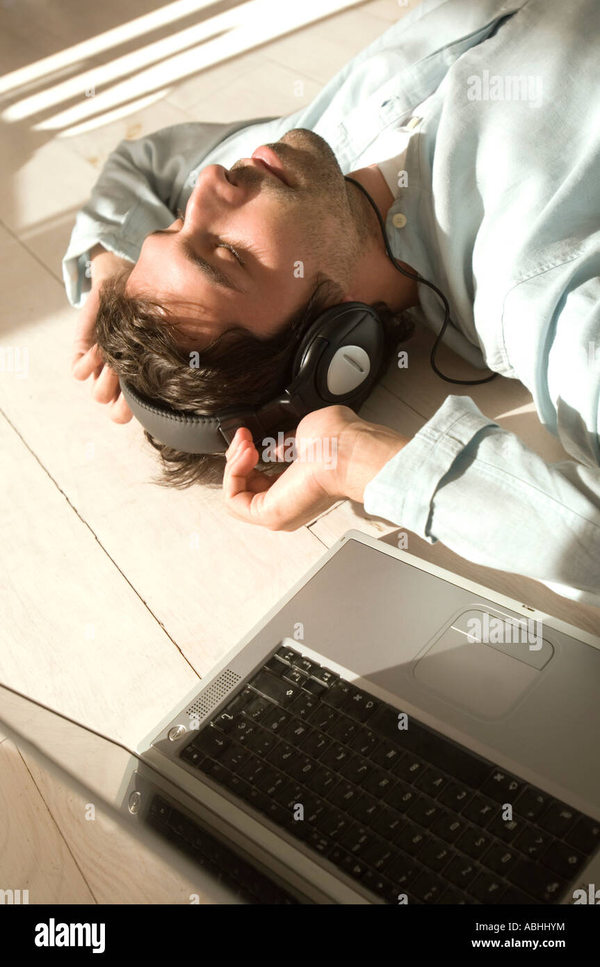 Junger Mann auf Boden liegend, Musikhören mit laptop Stockfoto