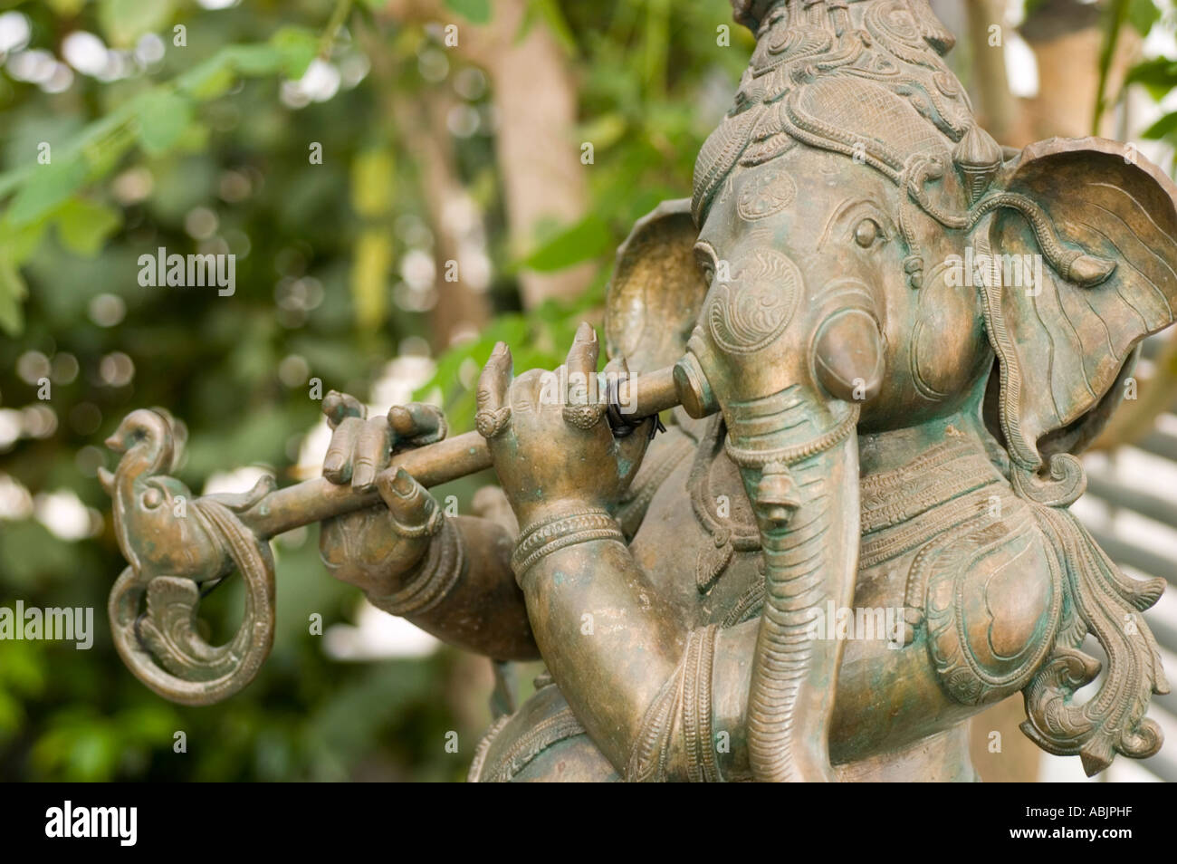 Felsskulptur des hinduistischen Elefantengottes Ganesh oder Ganesha, der eine Flöte in einem üppig grünen Garten spielt. Stockfoto