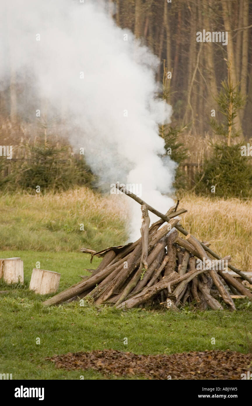 Dicker weißer Rauch steigt aus einem Lagerfeuer oder Lagerfeuer auf einem grasbewachsenen Feld mit dichtem Wald im Hintergrund auf. Stockfoto