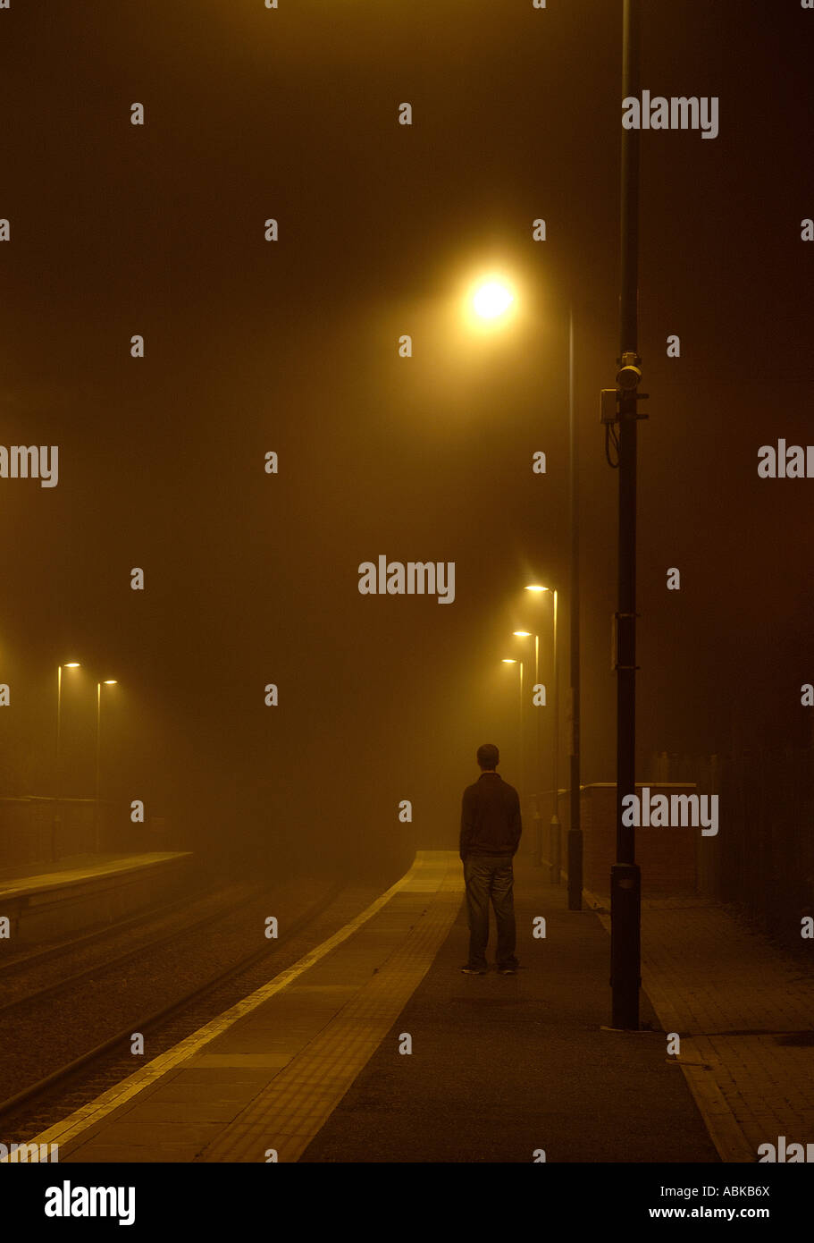 Ein Mann steht erwartungsvoll an einem nebligen Bahnhof. Stockfoto