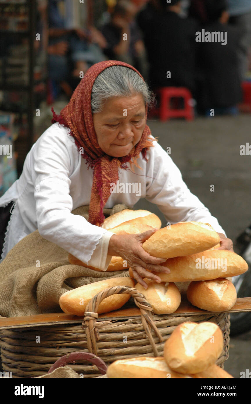 Eine ältere Frau stapelt Baguettes in einem Korb zum Verkauf in Hanoi in Vietnam. Stockfoto