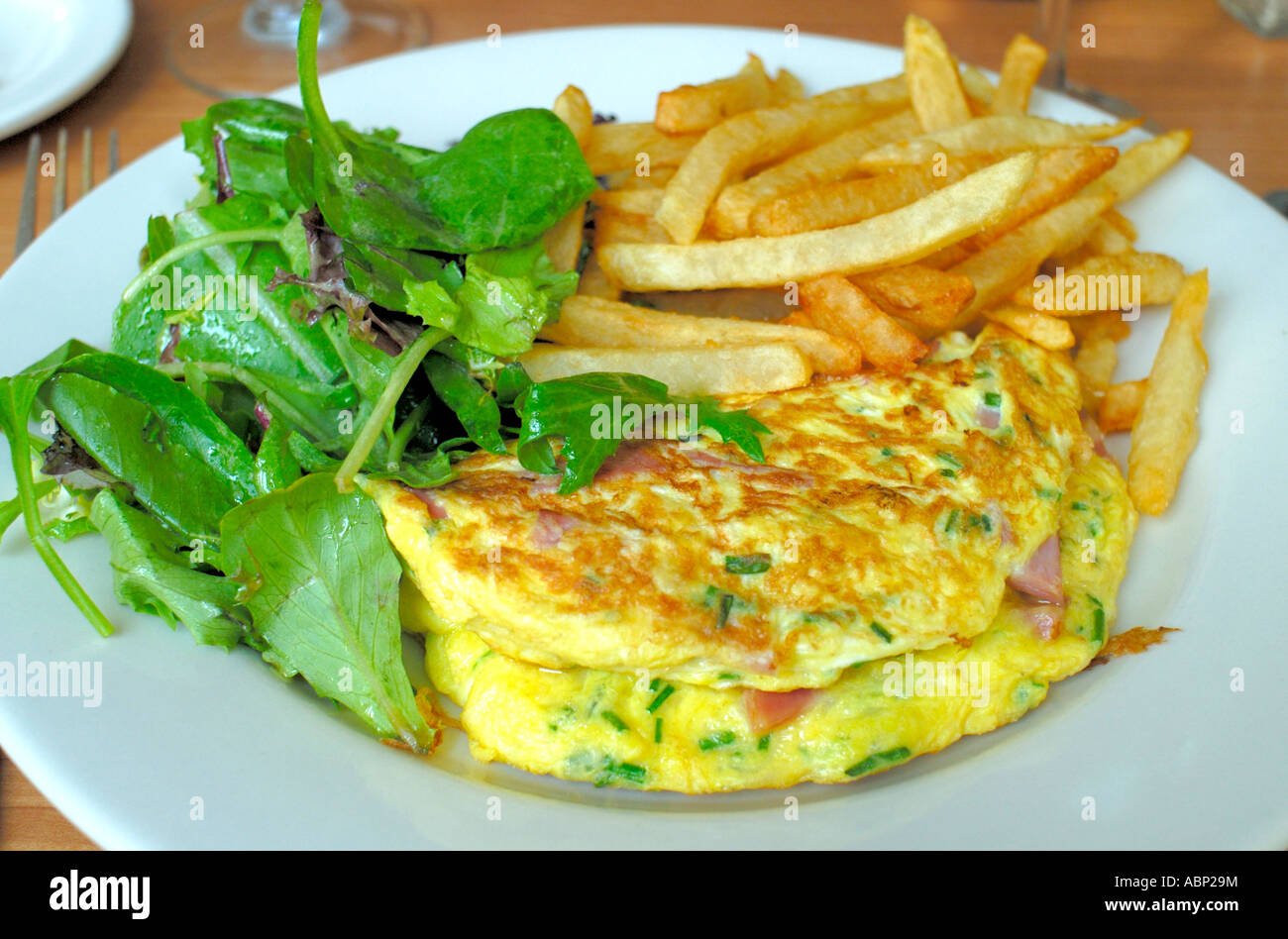 Ein Omelett mit Schinken, Käse und Kräutern begleitet von Pommes Kartoffeln und grünem Salat Omelett Stockfoto