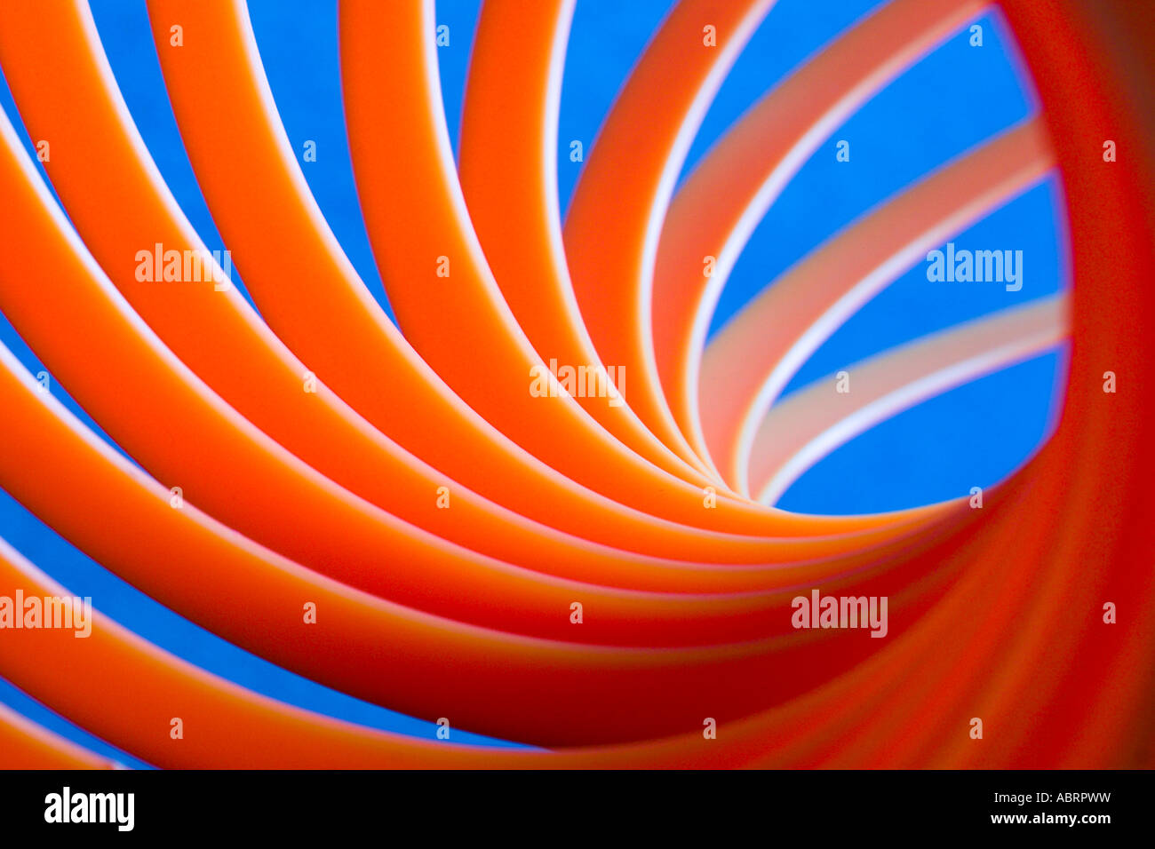 Leuchtend orange Kunststoff-Spirale Slinky vor blauem Hintergrund. Stockfoto
