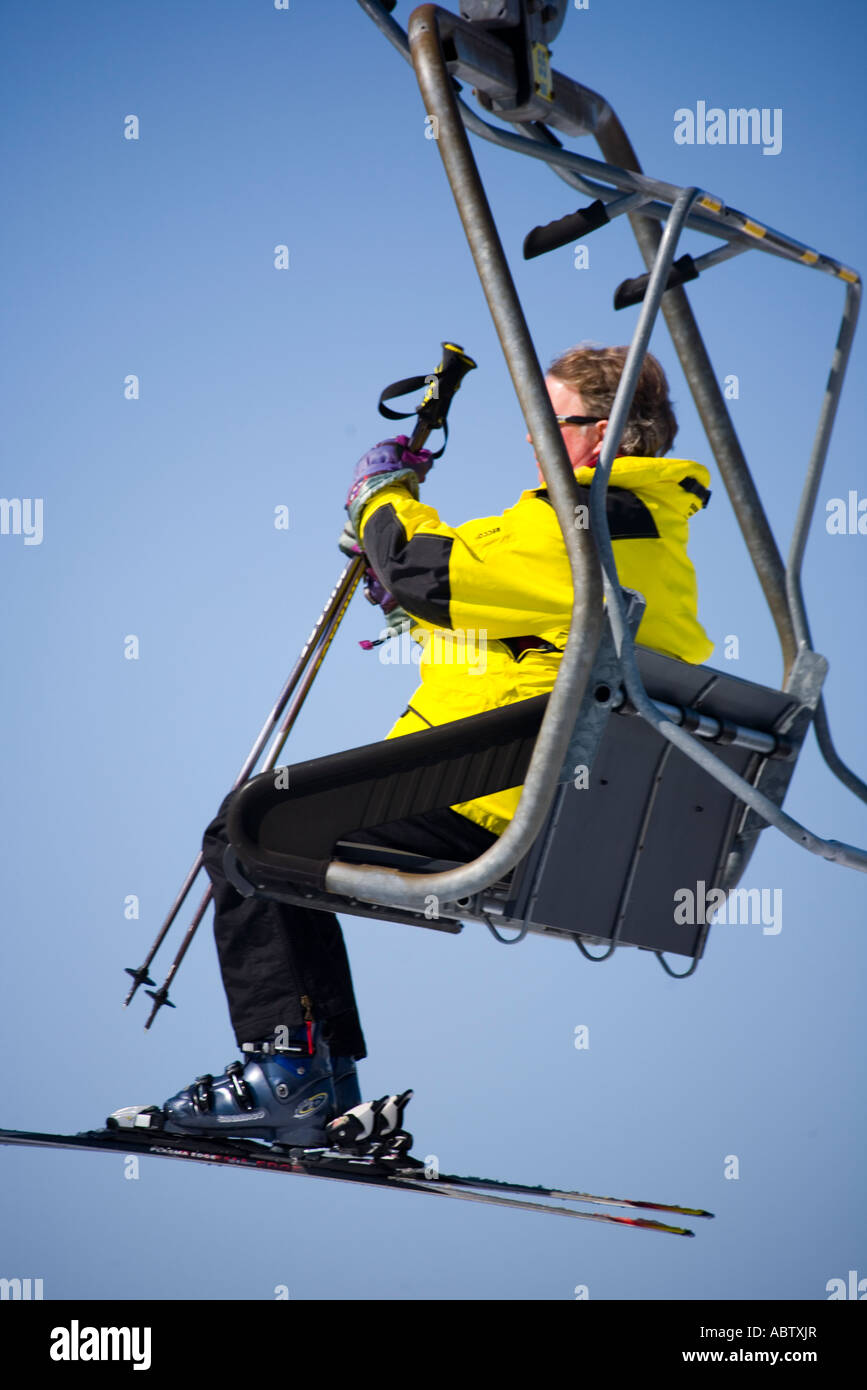 Mann in einer gelben Skijacke bereit, den Sessellift am oberen Rand der Piste aussteigen Stockfoto