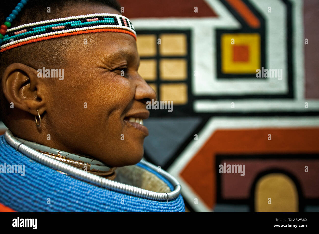 Ndebele-Frau in traditioneller Tracht mit traditionellen geometrischen Wandmalereien der Ndebele Dorf Modell freigegeben Südafrika Stockfoto