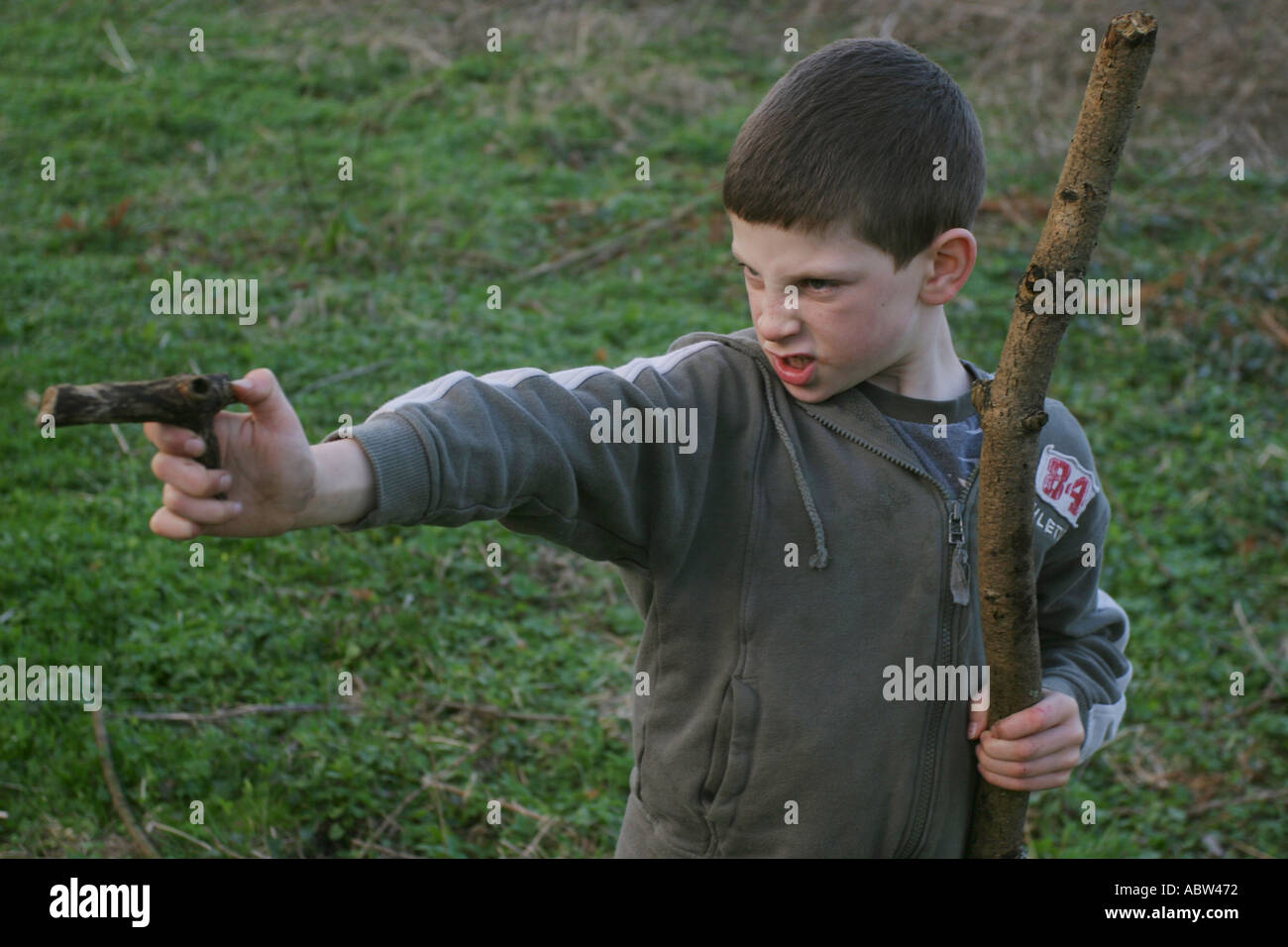 Ein 6-jähriger Junge benutzt einen Stock als Waffe während des Spielens, UK. Stockfoto