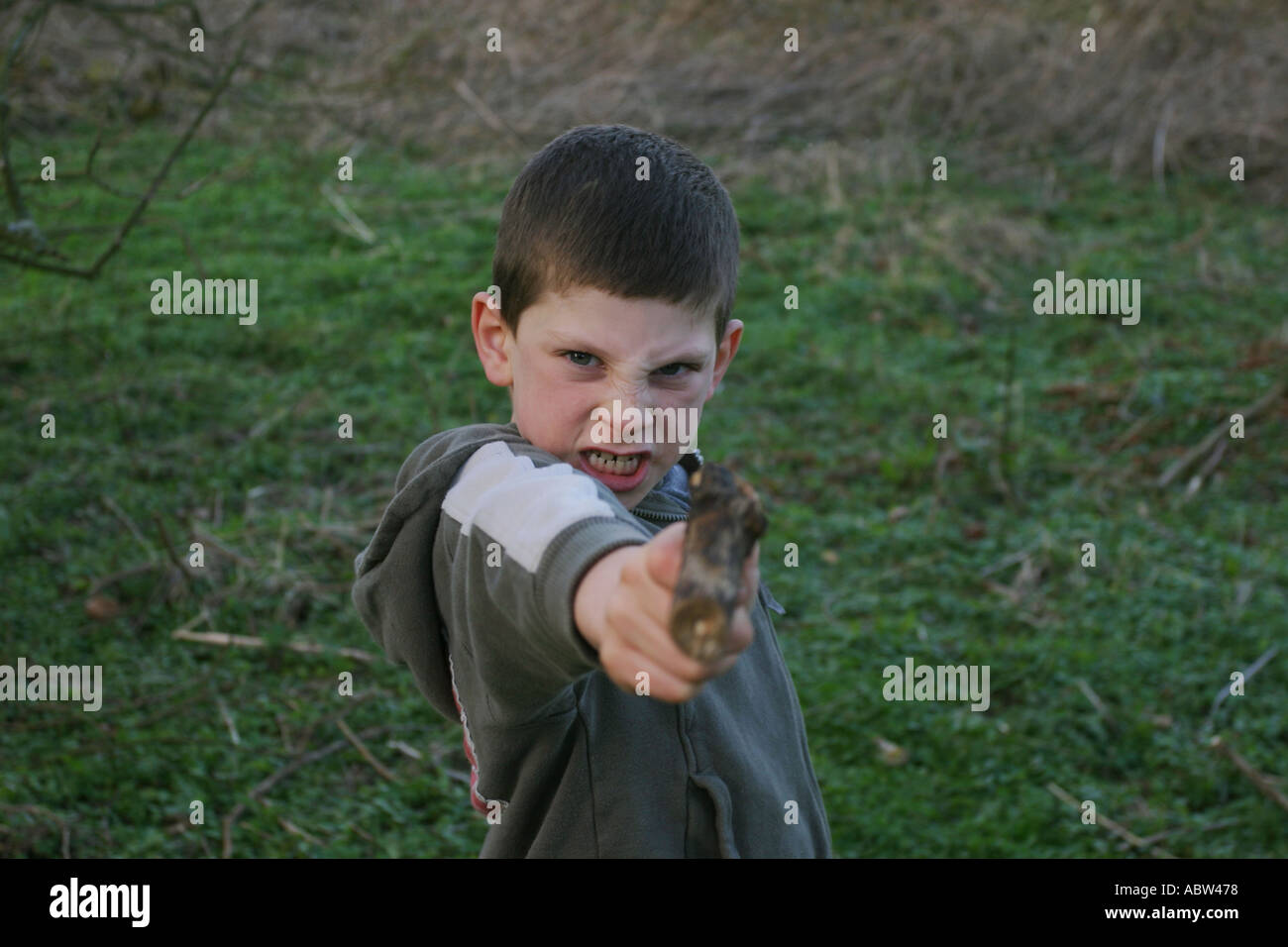 Ein 6-jähriger Junge benutzt einen Stock als Waffe während des Spielens, UK. Stockfoto