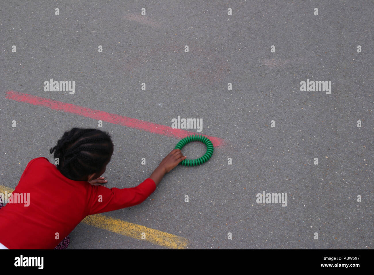 Eine Mädchen spielt mit einem kleinen Reifen in ihrer Schule Spielplatz, Betty Layward Primary School, London, Großbritannien. Stockfoto