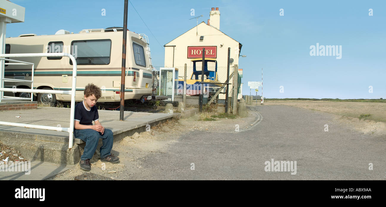 Junge sitzt allein durch den Straßenrand mit Wohnmobil und ein Hotel im Hintergrund Stockfoto