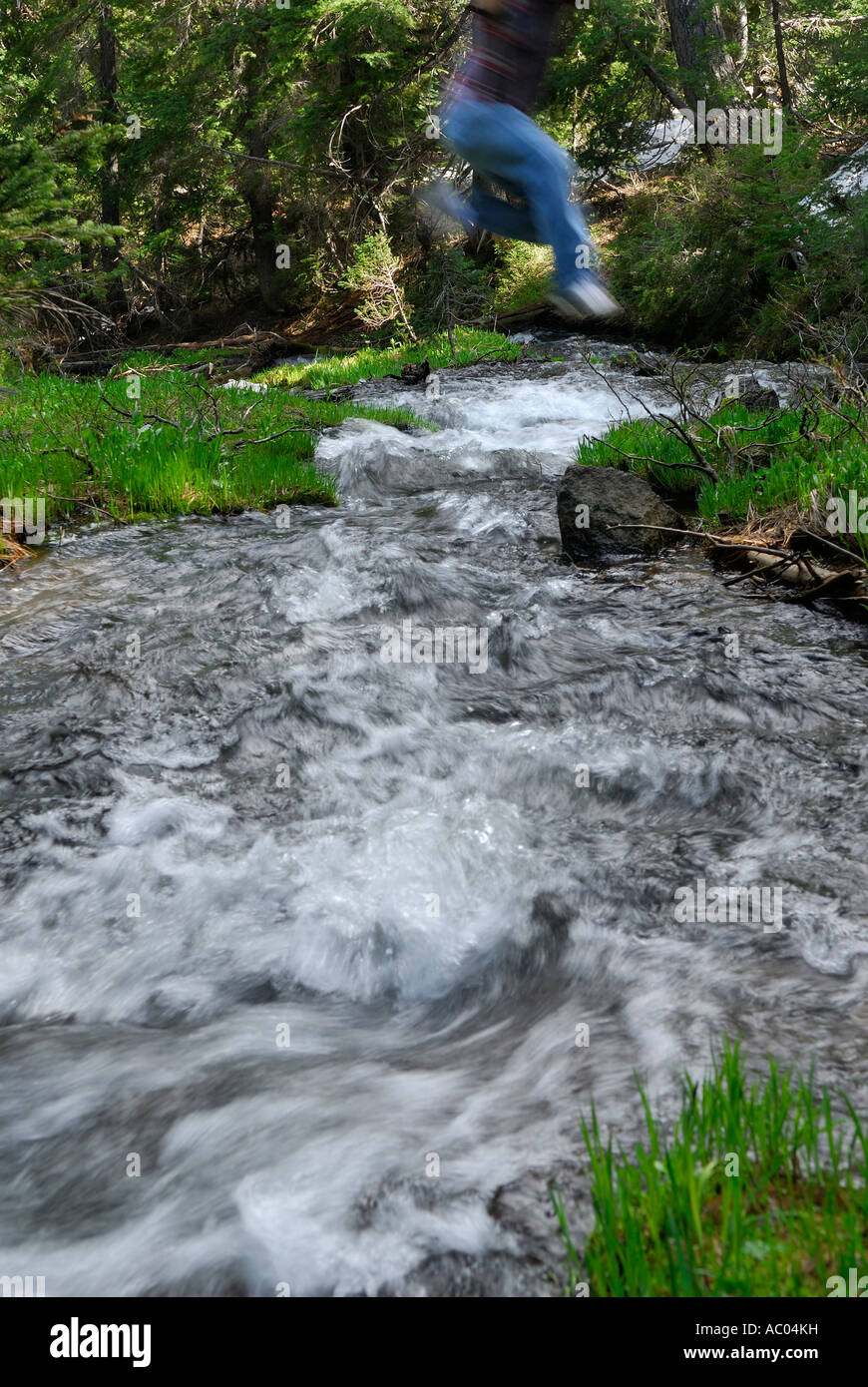 Mann, springen über einem kalten Gebirgsbach Stockfoto