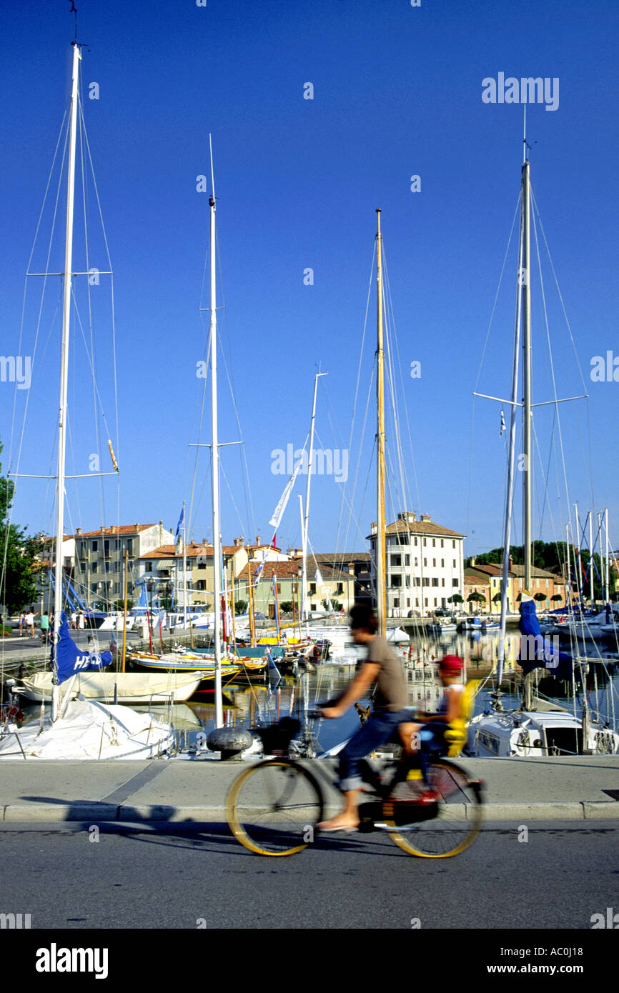 Eine Frau und Kind radeln vorbei an Boote in der Marina in Grado, Italien. Stockfoto