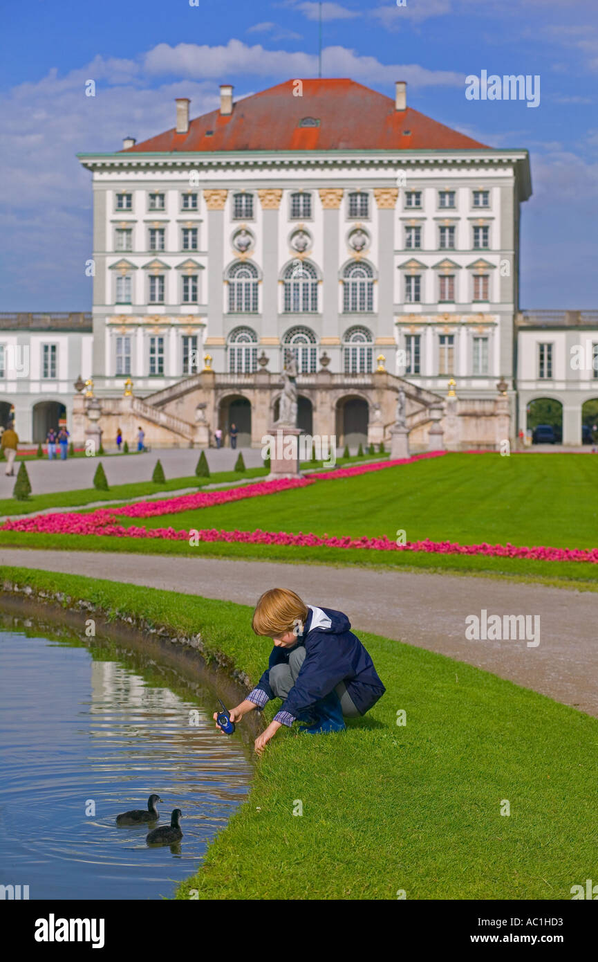 JUNGEN SPIELEN MIT ENTEN AUF DEM TEICH VOR SCHLOSS NYMPHENBURG MÜNCHEN BAYERN DEUTSCH Stockfoto