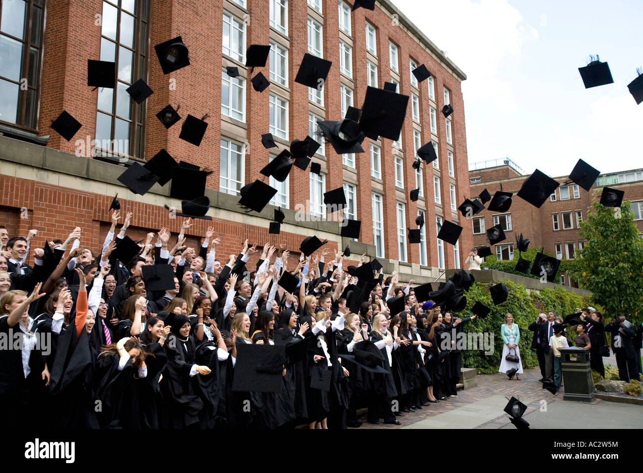 Absolventinnen und Absolventen werfen ihre Mörtel-Boards in der Luft an der Graduierung Tag, Universität von Birmingham, England, UK. Stockfoto