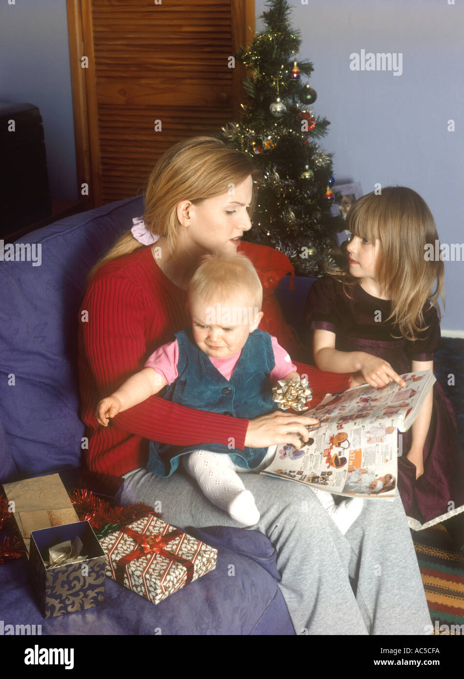 Mutter mit ihren Kindern auf der Suche in einem Katalog für Spielzeug und Geschenke, belästigt zu werden Stockfoto