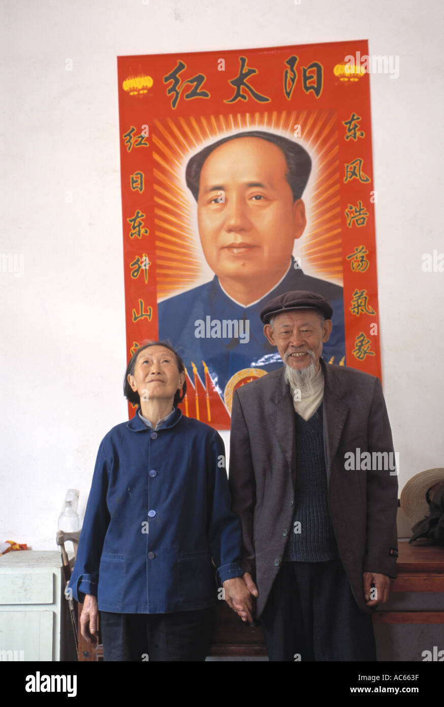 Ein indoor-Porträt von einem senior chinesisches Ehepaar vor dem Plakat des Vorsitzenden Mao in der Nähe von Zigui China Stockfoto