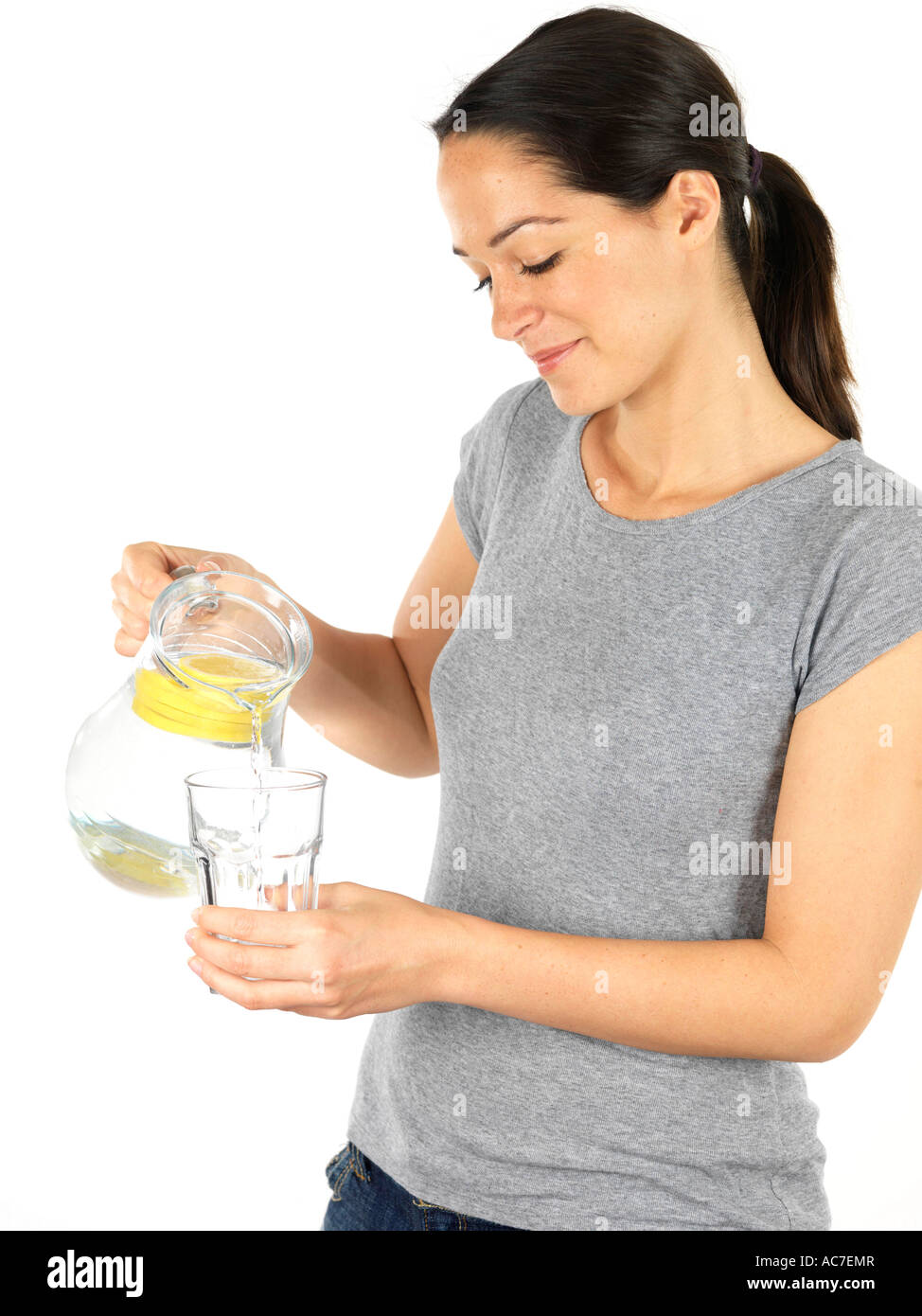 Glückliche junge Frau mit und gießt Frisches erfrischendes Wasser in ein Glas aus dem Krug Isoliert gegen einen weißen Hintergrund mit einen Freistellungspfad Stockfoto
