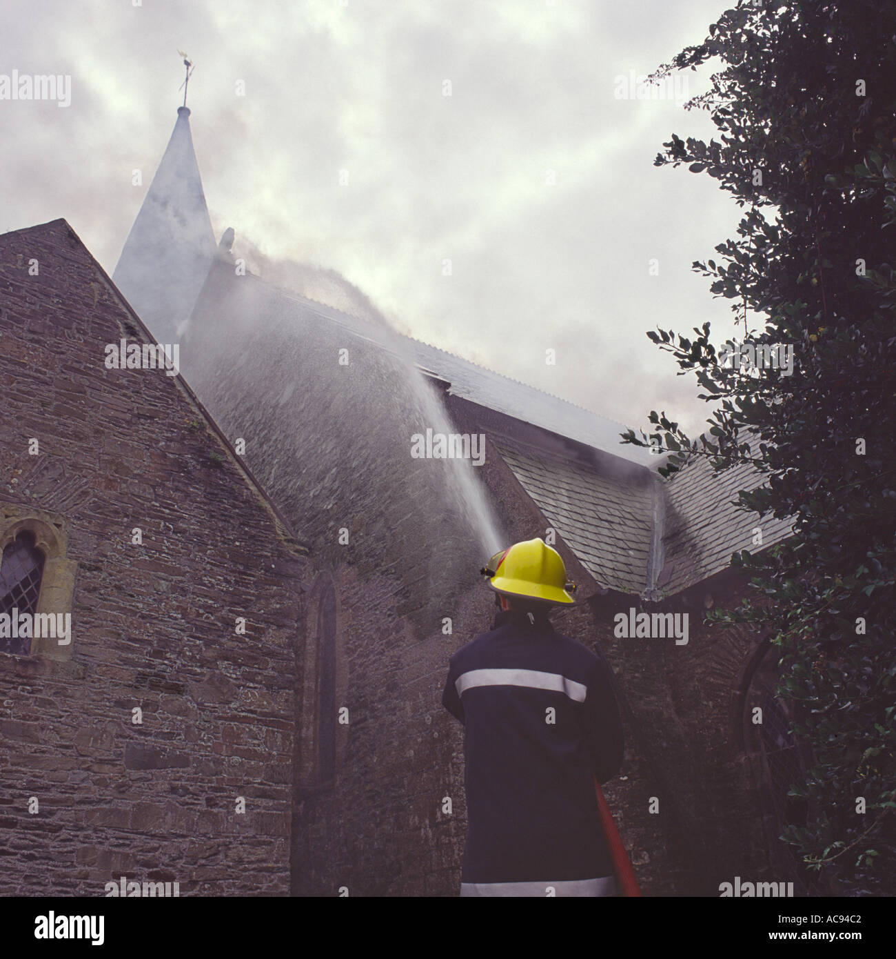 Feuerwehrmann Schlauch nach unten Dach Brandgefahr durch Kleinkinder an der St. Brannocks Kirche Braunton North Devon in England Stockfoto