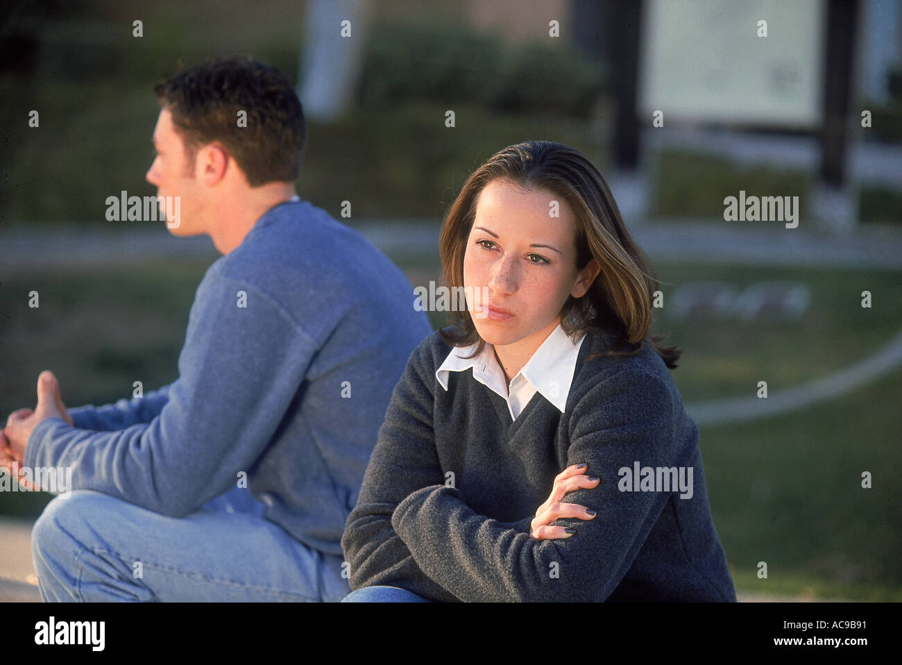 Zwei Teenager sitzen unter einem Baum nach entgegengesetzten Richtungen Stockfoto