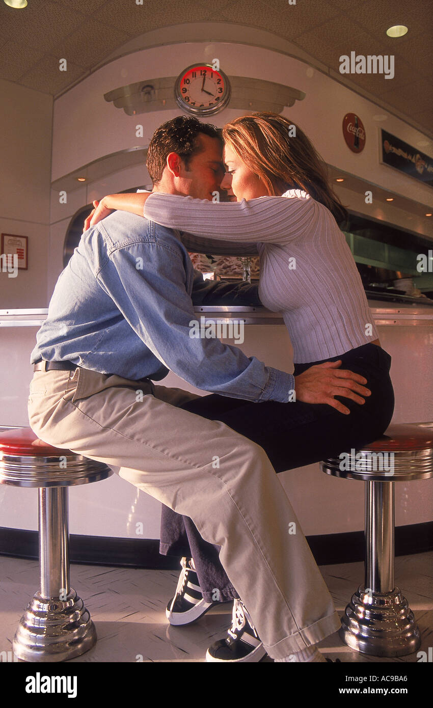 Ein paar im 50er Jahre Diner sitzen auf Soda Jerk Hocker gegenüber jeder anderen umarmen küssen Stockfoto