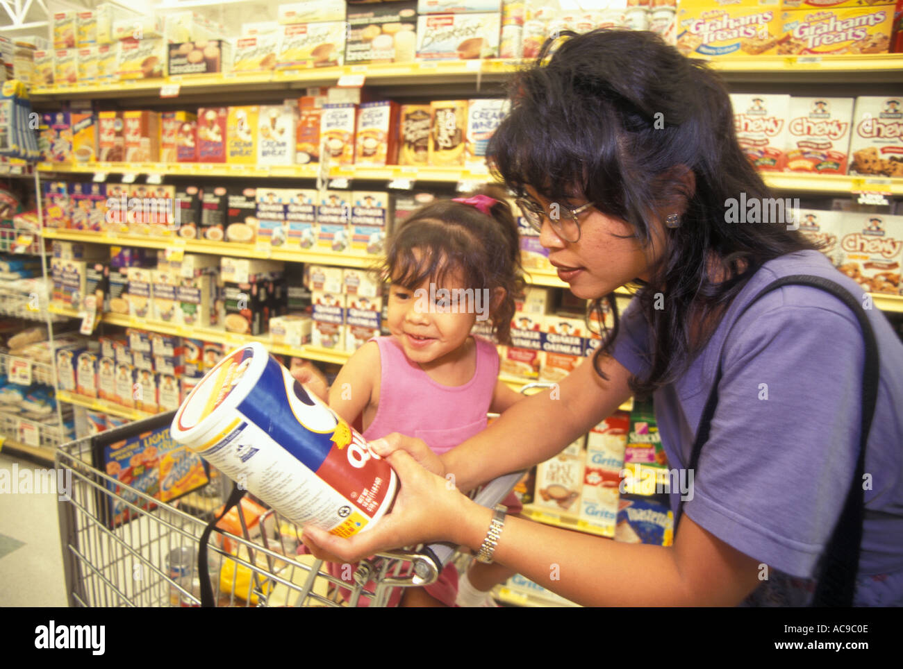 Asiatische amerikanische Frau mit Tochter sitzen Warenkorb lesen Bestandteile von Quaker Oats. Mutter Unterrichten junger Mädchen. © HERR Myrleen Pearson Stockfoto