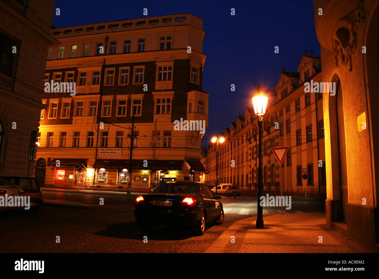 Nachtblick auf eine ruhige Straße in Prag mit historischen Gebäuden, die von Straßenlaternen beleuchtet werden, und einem Auto, das auf der Kopfsteinpflasterstraße parkt. Stockfoto