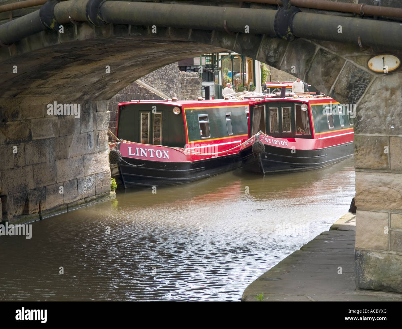 Zwei rot bemalten schmalen Kanalboote unter eine gewölbte Brücke am Leeds-Liverpool-Kanal in Skipton West Yorkshire gesehen Stockfoto