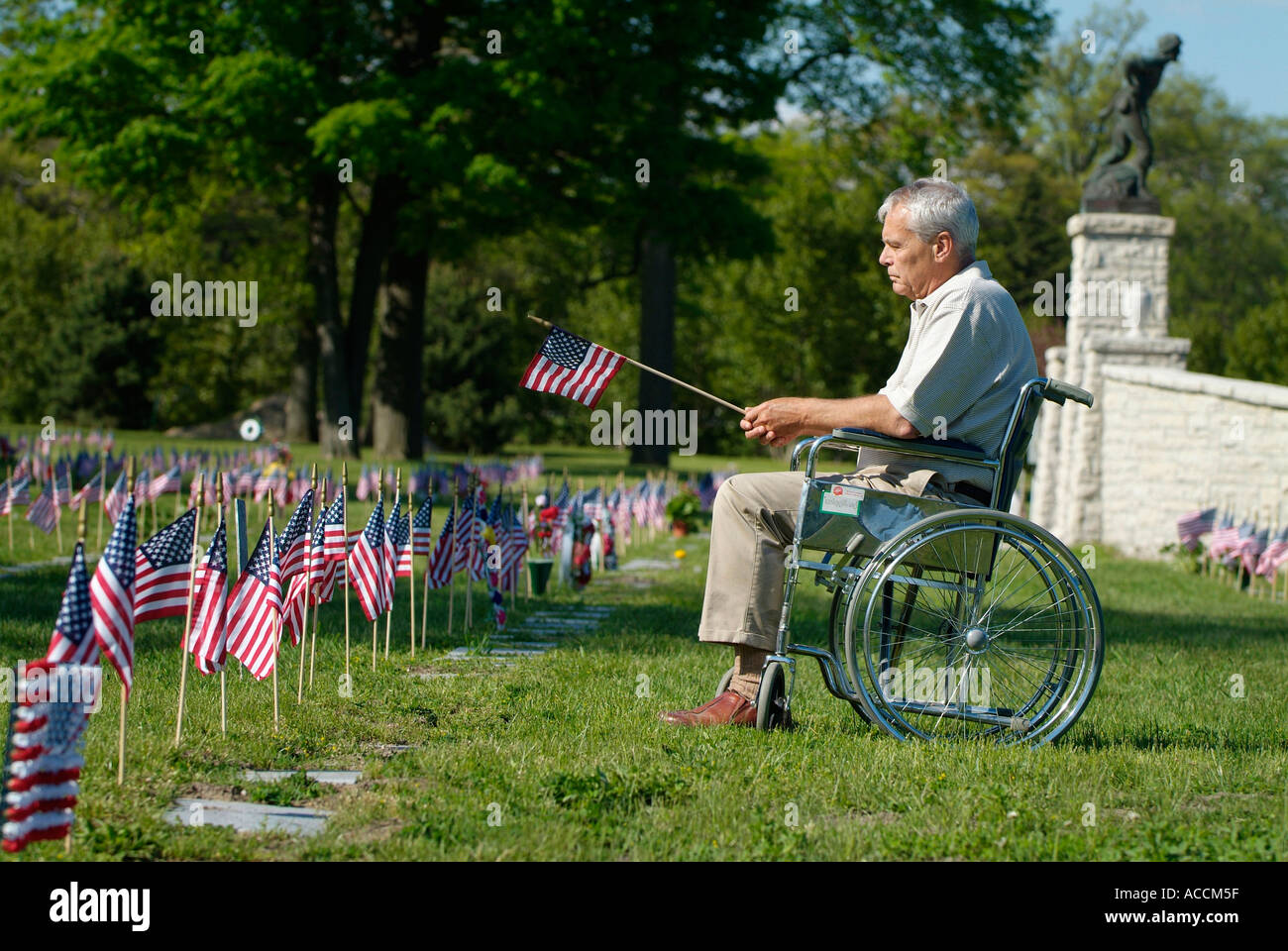 Behinderte Senioren männlich sitzt im Rollstuhl mit Fahne in der Hand am Memorial Day am Friedhof Stockfoto