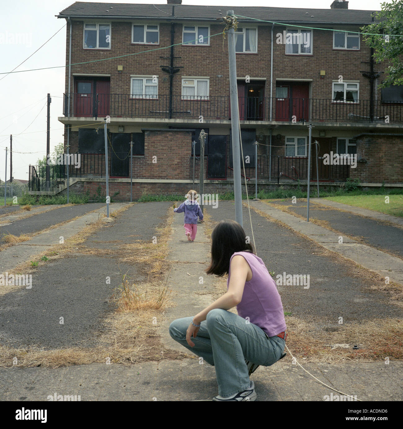 Ein junges Mädchen spielt in einer Sozialsiedlung beobachtet von ihrem allein erziehenden Elternteil, eine junge Mutter, Bristol, UK. Stockfoto