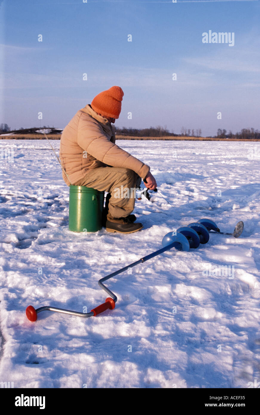 Ein Eis angeln Enthusiast darauf wartet, von seinem Loch im Eis auf einem gefrorenen Minnesota See. Stockfoto